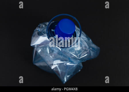 Crumpled pressed blue plastic pet water bottle as recycling single use pollution waste ecology nature concept isolated on black background Stock Photo