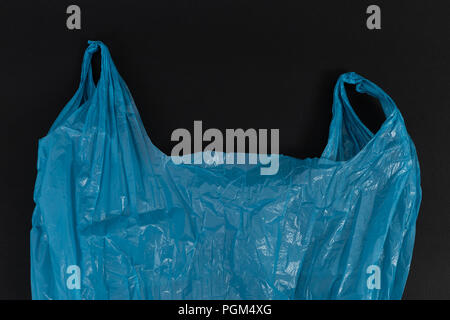 Used crumpled single use blue plastic bag with handles as waste pollution environment ecology concept isolated on black background Stock Photo