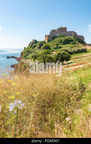 Wild flowers fill the foreground with Mont Orgueil Castle above the town of Gorey on the island of Jersey in the background. Taken on a summers day. Stock Photo