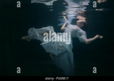 Beautiful woman in a white dress swims under the water. Stock Photo