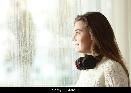 Side view portrait of a distracted teen at home looking outdoors in a rainy day Stock Photo