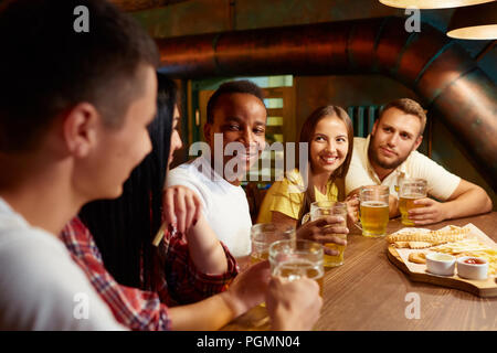Company of friends speaking and having drinking in bar. People sitting at wooden table with beers and snacks, communicate, having fun together, everyo Stock Photo