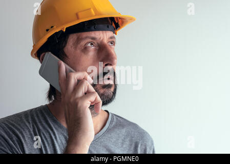 Construction engineer talking on mobile phone, serious adult male person using smartphone for communication with workers on building site Stock Photo