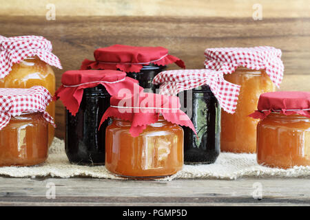 Variety of homemade jams and preserves covered with checkered and red cloth against a rustic background. Extreme shallow depth of field with selective Stock Photo