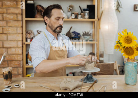 Dark-haired bearded potter feeling busy working with pottery wheel Stock Photo