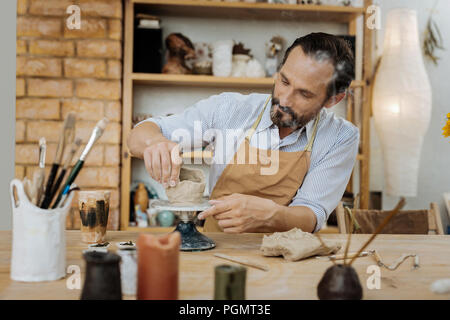 Bearded potter feeling happy while working in his workshop Stock Photo