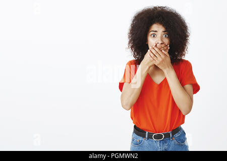 Portrait of shocked worried attractive african-american female sibling with afro haircut, covering mouth with both palms, staring terrified at camera, being speechless from anxiety and shock Stock Photo