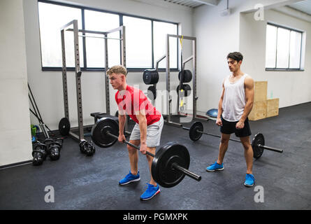 Young handsome fit men in gym working out, lifting bar of barbell, flexing muscles. Stock Photo