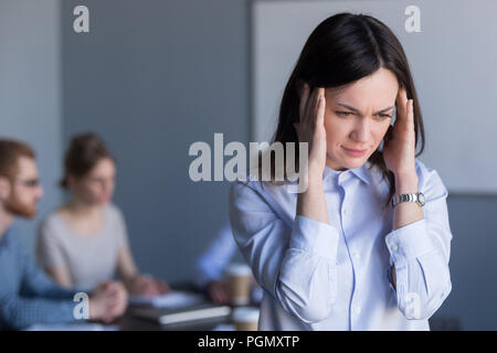 Stressed female worker suffer from headache during office meetin Stock Photo