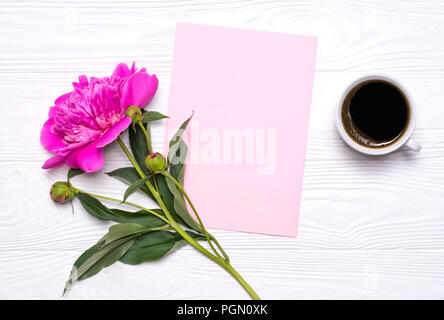 Empty paper with place for text, a cup of coffee and peony flower on a white wooden background. Mockup for your design. View from above. Stock Photo