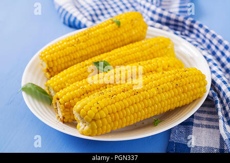 Boiled corn in white plate on blue background. Summer food. Stock Photo