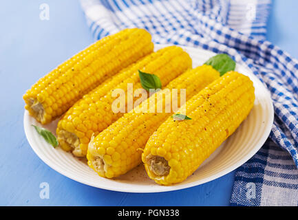 Boiled corn in white plate on blue background. Summer food. Stock Photo