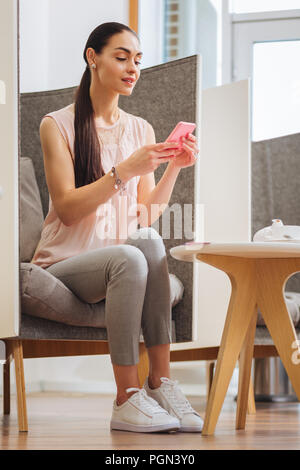 Delighted positive young woman using her smartphone Stock Photo