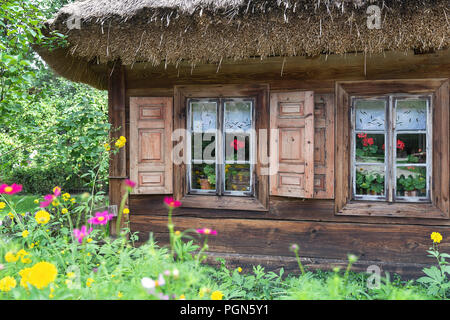 Old wooden house with widnow shutters and surrounded by flowers and trees Stock Photo