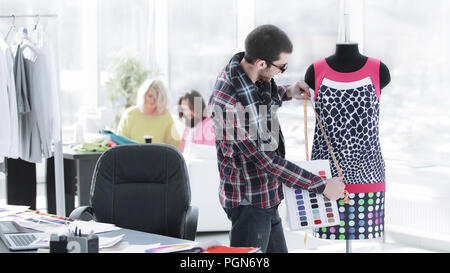 handsome fashion designer sitting with clothing sketches at the studio full of tailoring tools and clothes Stock Photo