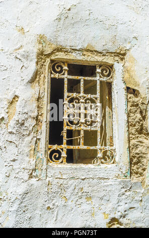The old wall with crumbling plaster and rusty grill on tiny window, Sfax, Tunisia. Stock Photo
