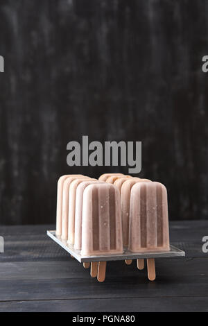 Frozen coffee drink on a stick in plastic form on a black wooden background with space for text. Cold flying dessert Stock Photo