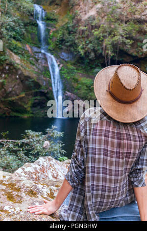 Back view of young girl in straw hat and looking at waterfall. Caucasian young lady looks at falling water, photo on fresh air. youth adolesce in wild nature Stock Photo