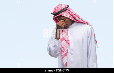 Young arabic african man wearing traditional keffiyeh over isolated background tired rubbing nose and eyes feeling fatigue and headache. Stress and fr Stock Photo