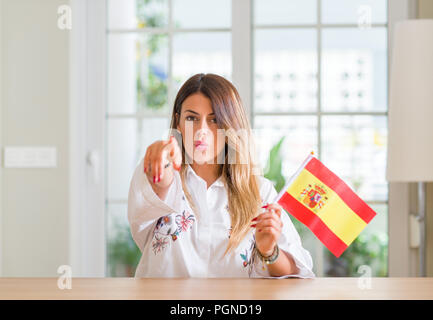 Young woman at home holding flag of Spain pointing with finger to the camera and to you, hand sign, positive and confident gesture from the front Stock Photo