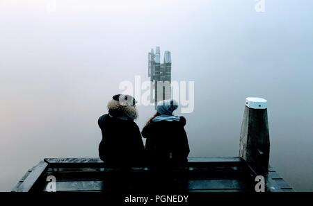 Couple on wooden jetty on a lake in holland surrounded by fog Stock Photo