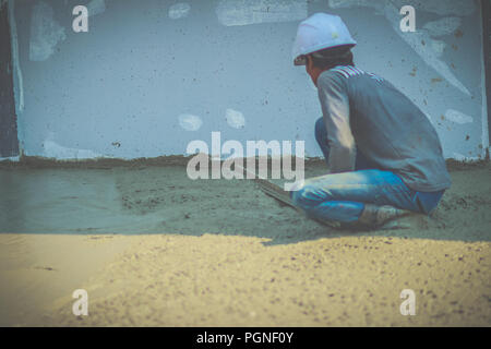 Masonry worker is using long trowel to smooth or leveling concrete flooring work step of the building construction. Stock Photo