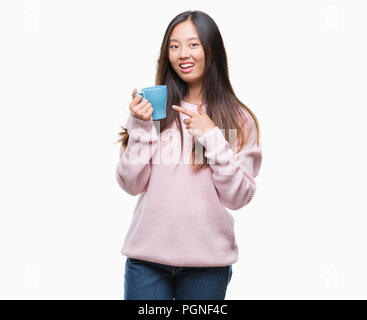 Young asian woman drinking coffee over isolated background very happy pointing with hand and finger Stock Photo