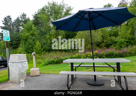 An outdoor designated smoking area near a building in New Hartford, NY USA with picnic table, umbrella, trash can, and a collection of cigarette butts. Stock Photo