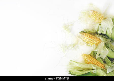 Fresh yellow sweet corn cobs on white table background. Vegetable decorative frame composition, web banner. Flat lay, top view. Stock Photo