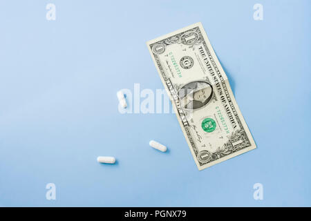 White pills with money on light blue pastel background desk. Stock Photo