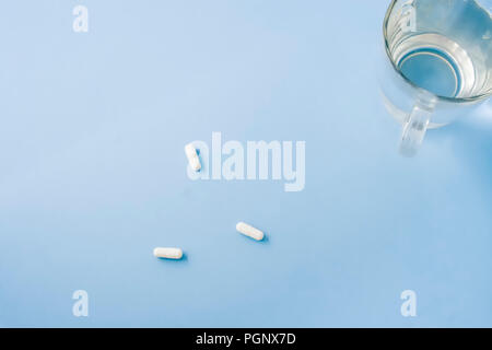 White pills with a cup of fresh water placed on pastel blue table. Flat lay, top view. Stock Photo