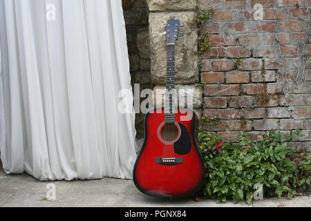 Groom's red and black guitar leaning against the wall on the wedding ceremony. Stock Photo