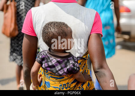 KUMASI, GHANA - JAN 15, 2017: Unidentified Ghanaian little girl is carried by her mother at the Kumasi market. Ghana children suffer of poverty due to Stock Photo