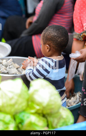 KUMASI, GHANA - JAN 15, 2017: Unidentified Ghanaian little boy stands near the basin with fish at the Kumasi market. Ghana children suffer of poverty  Stock Photo