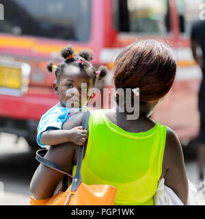 KUMASI, GHANA - JAN 15, 2017: Unidentified Ghanaian baby girl is carried by her mother at the Kumasi market. Ghana children suffer of poverty due to t Stock Photo