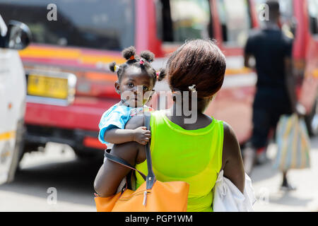 KUMASI, GHANA - JAN 15, 2017: Unidentified Ghanaian baby girl is carried by her mother at the Kumasi market. Ghana children suffer of poverty due to t Stock Photo