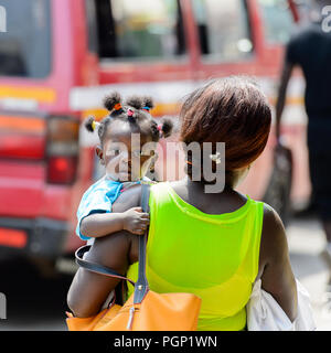 KUMASI, GHANA - JAN 15, 2017: Unidentified Ghanaian baby girl is carried by her mother at the Kumasi market. Ghana children suffer of poverty due to t Stock Photo