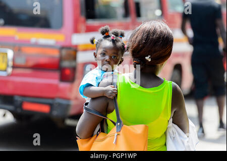 KUMASI, GHANA - JAN 15, 2017: Unidentified Ghanaian baby girl is carried by her mother at the Kumasi market. Ghana children suffer of poverty due to t Stock Photo