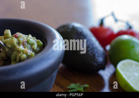 Making guacamole in a mortar with the ingredients showing on the background Stock Photo