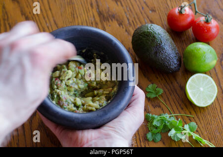 Making guacamole in a mortar with the ingredients showing on the background Stock Photo