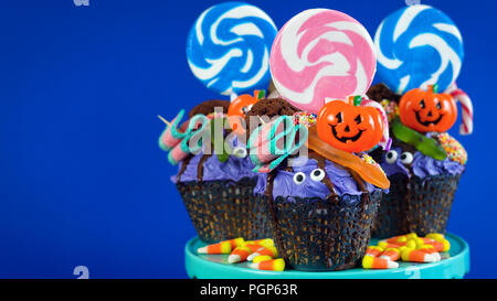 Happy Halloween candyland drip cake style cupcakes with lollipops and candy on blue background. Stock Photo