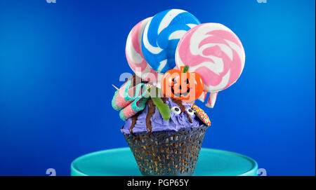 Happy Halloween candyland drip cake style cupcakes with lollipops and candy on blue background. Stock Photo