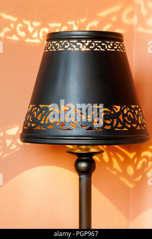 Morocco pierced dark metal design lamp shade, casting shadows on the orange wall. Example of Moroccan decorative style. Location: Marrakech. Stock Photo
