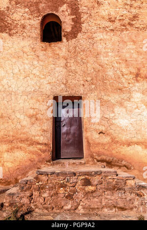 Morocco rustic plaster wall with stone steps leading to a small metal door. Open arched window above. Rich ocher colors. Patina of age. Vertical. Stock Photo