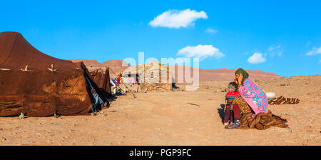 Nomad child and mother speaking on a cell phone in the Sahara desert in Morocco on Dec. 28, 2012. Their tent is made of woven camel hair. Stock Photo