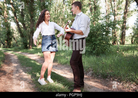 young couple walking in the forest, playing guitar and dancing, summer nature, bright sunlight, shadows and green leaves, romantic feelings Stock Photo