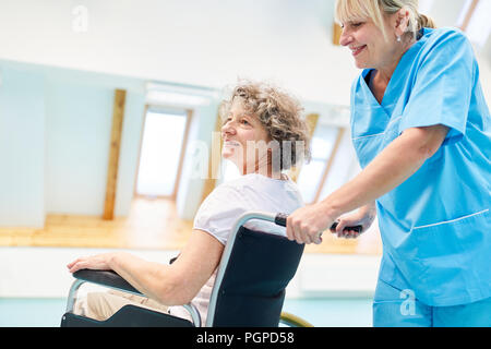 Caregiver cares for a senior woman in a wheelchair in physiotherapy Stock Photo