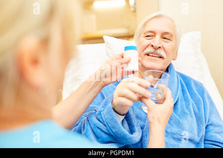 Caregiver or nurse distributes tablets to sick senior man Stock Photo