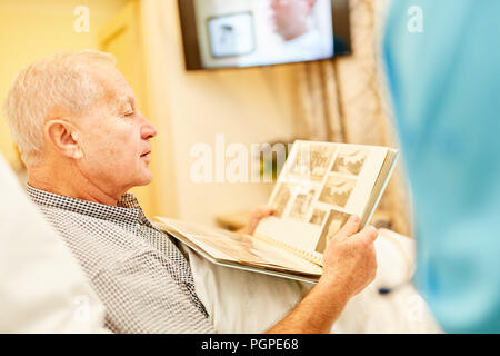 Old man with Alzheimer looks at a photo album at the retirement home Stock Photo