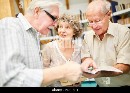 Three seniors enjoy learning through books in a library Stock Photo